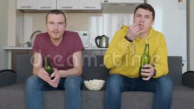 两个男人坐在沙发上看电视上的足球赛，喝啤酒，吃爆米花